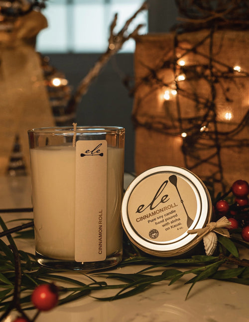 Ele Kauai Cinnamon Roll glass candle and 4 oz tin in festive greenery with warm lights
