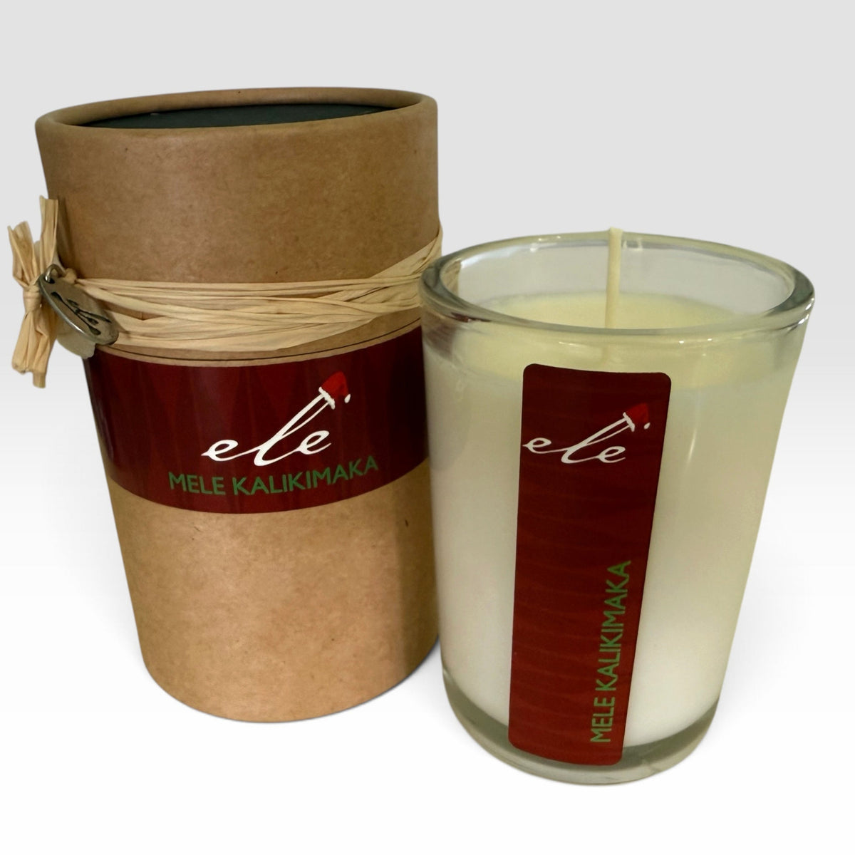 Mele Kalikimaka 7 oz glass candle and kraft gift tube on a clean light background